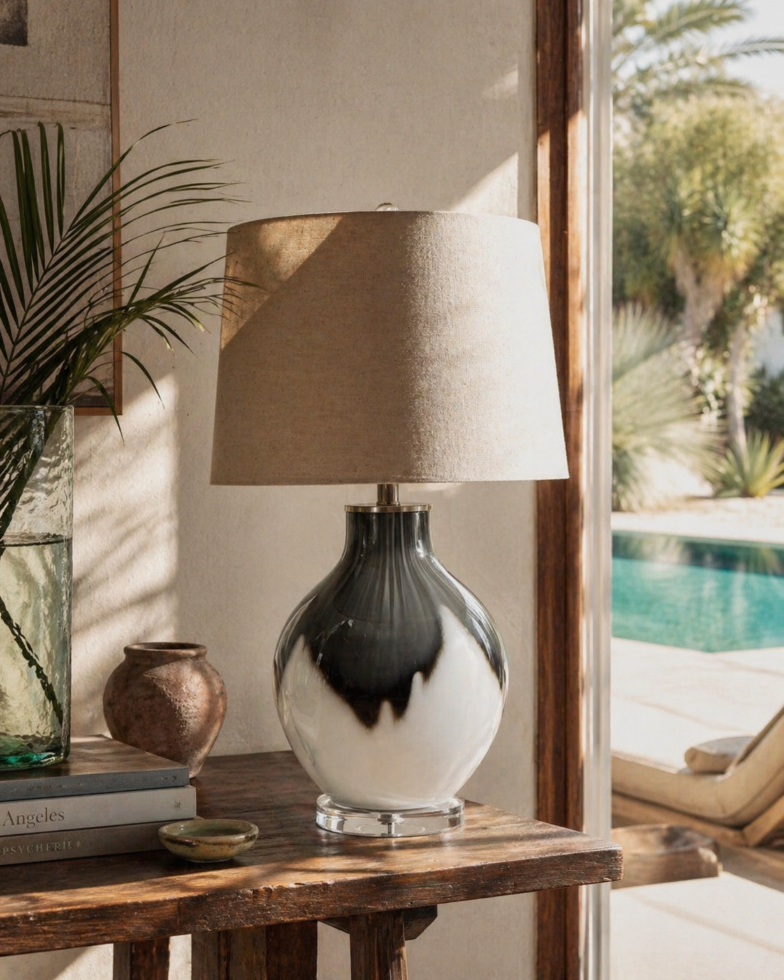 Decorative lamp on a wooden table with a view of a pool and outdoor furniture.