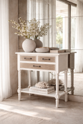 White console table with textured wooden drawer fronts styled against antiqued mirror tiles in a light-filled coastal luxury interior.