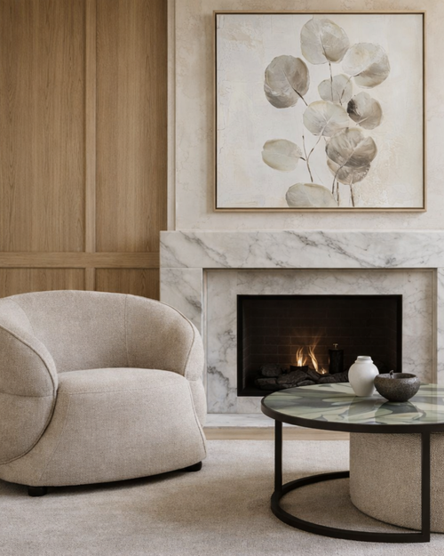 Modern living room with a beige armchair, marble fireplace, abstract artwork and round coffee table.