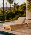 Beige lounge chair by a pool with palm trees and greenery in the background