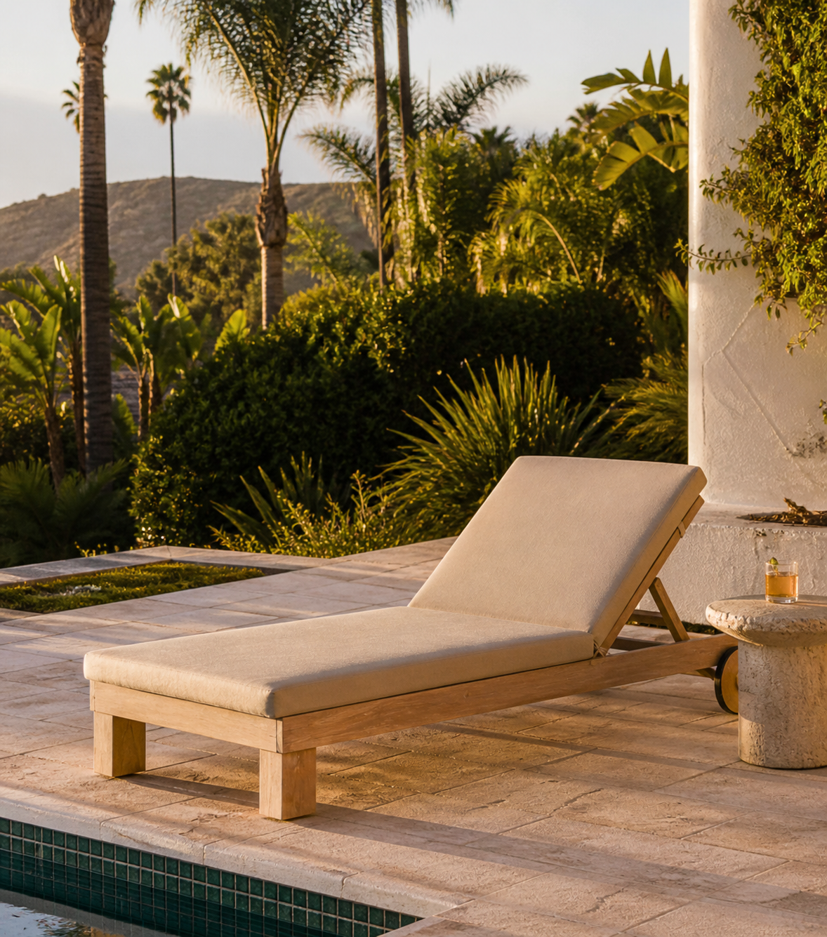 Beige lounge chair by a pool with palm trees and greenery in the background