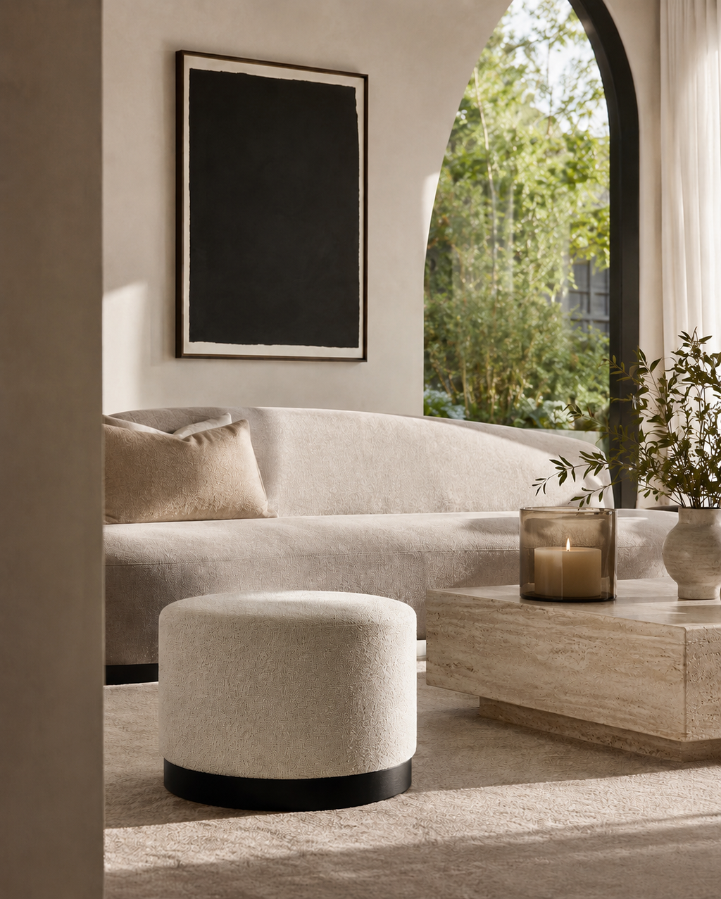Modern living room with a beige sofa, ottoman, and coffee table with a candle.