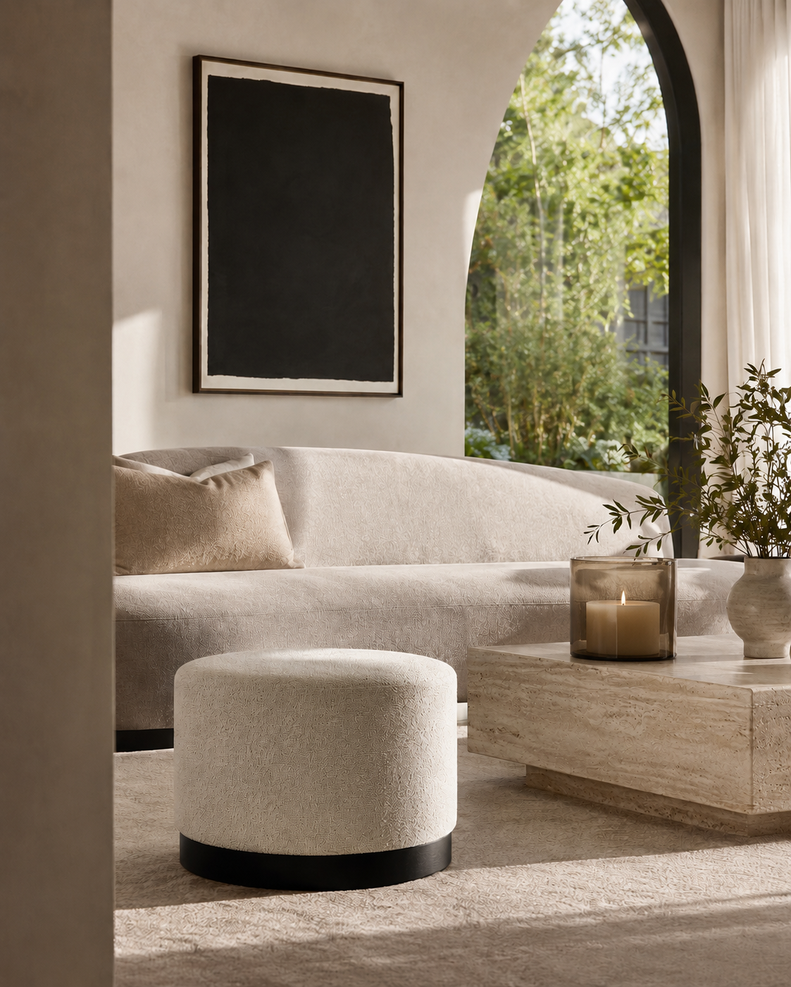 Modern living room with a beige sofa, ottoman, and coffee table with a candle.