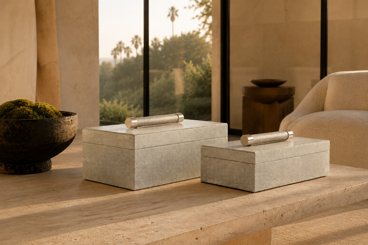 Two rectangular stone storage boxes with cylindrical metal handles sit on a wooden table in a modern interior setting with warm natural light.