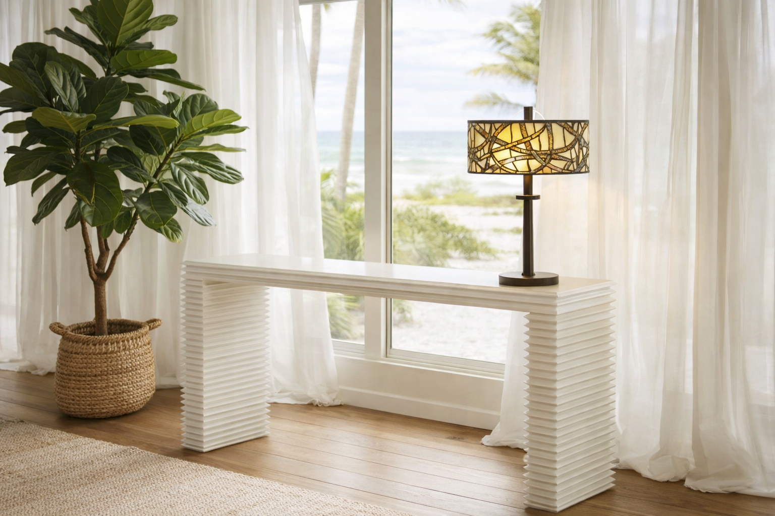 White textured console table with a lamp and plant in a bright room with large windows.
