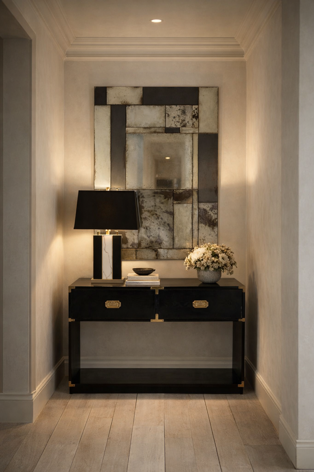 Decorative black mango wood console table with a marble table lamp and flowers against a wall with a large antique effect abstract mirror.