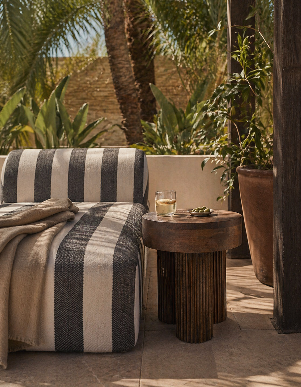 Striped blanket on a chair with a brown mango wood side table and drink in a garden setting