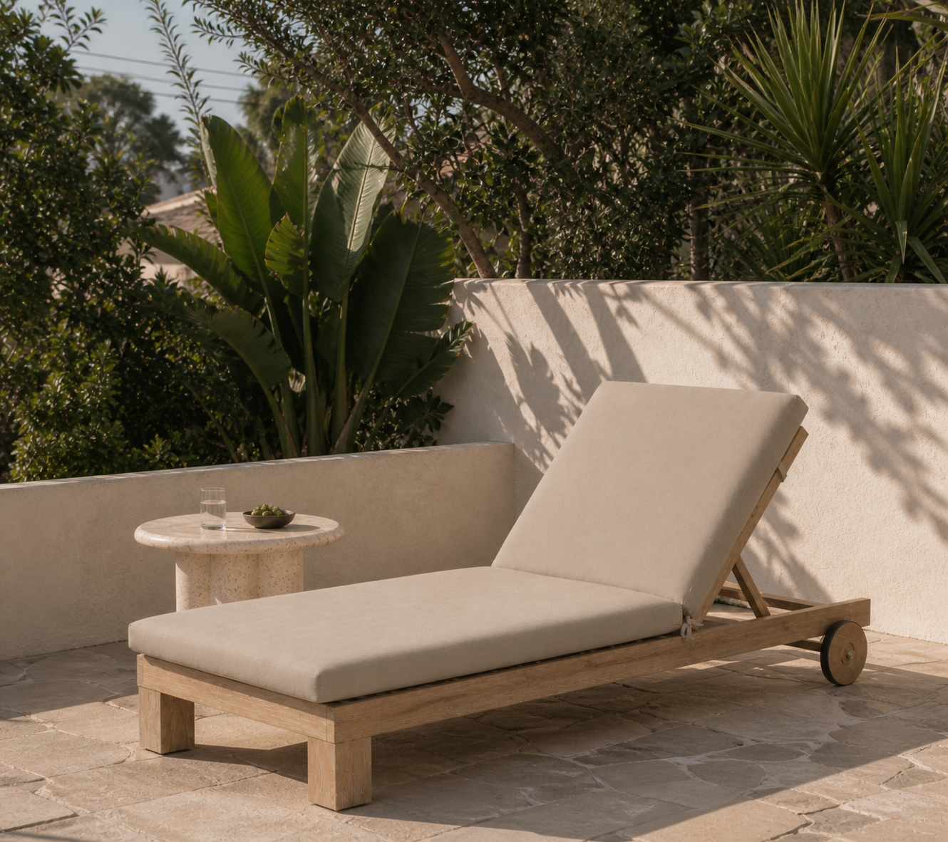 Beige lounge chair on a stone patio with a small table and plants in the background