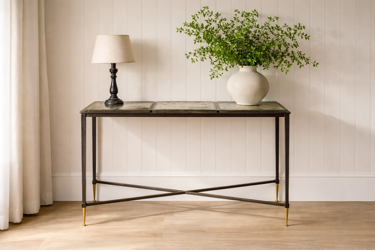 Console table with a vase of greenery and a lamp against a neutral wall.