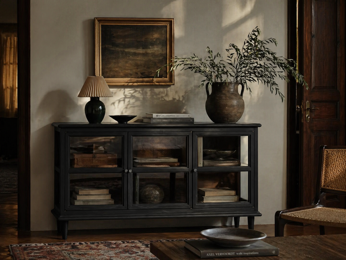 Dark wooden cabinet with decorative items in a room with a painting and lamp.