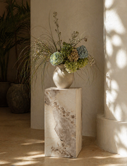 Decorative vase with flowers on a marble pedestal in a softly lit room.